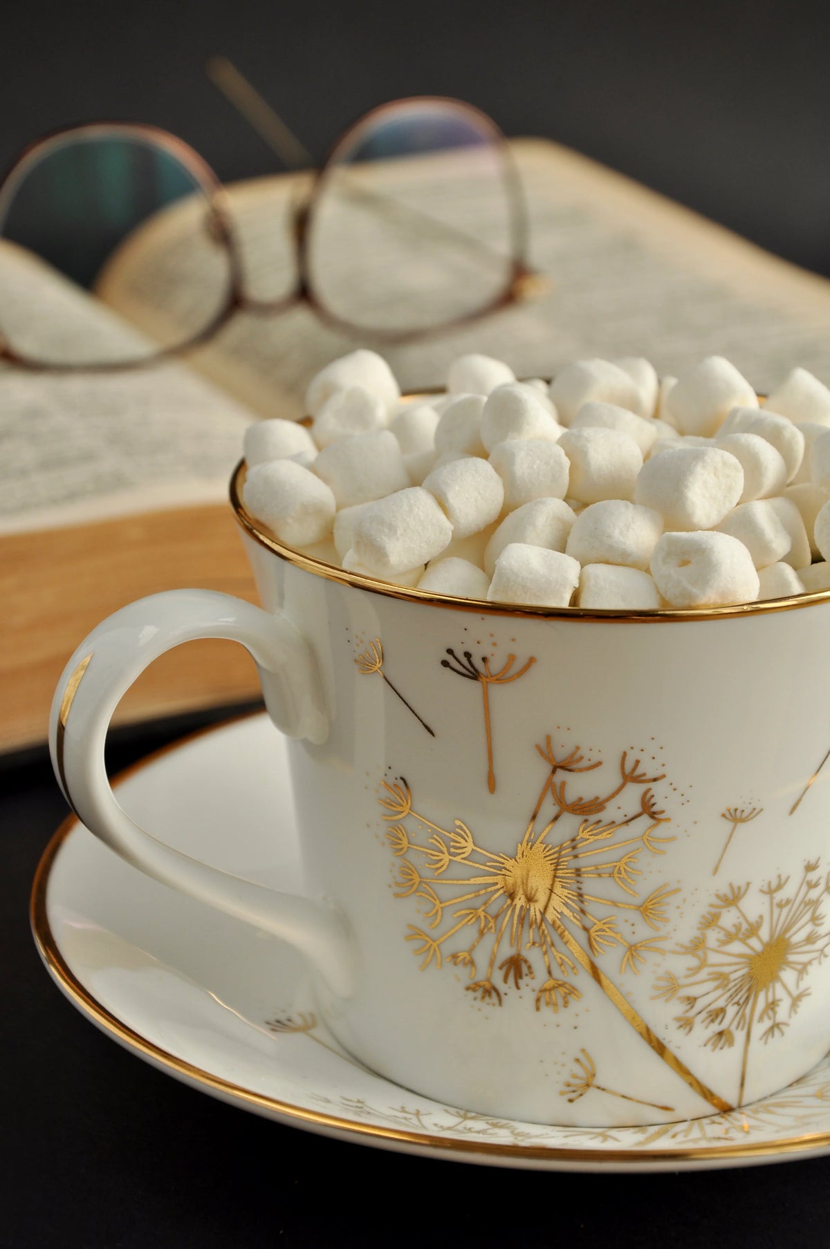 Generous dandelion cup filled with marshmallows with an open book and reading glasses in the background
